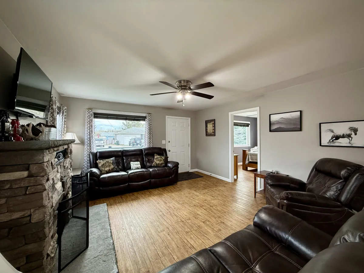 A comfortable living space with leather couches facing a fireplace and television, flanked by windows streaming in natural light. The arrangement fosters easy conversation and relaxation for family or group gatherings.