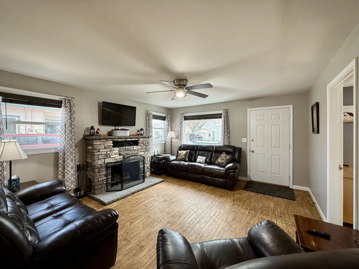 The image showcases a warm and inviting living room with a striking stone fireplace as the centerpiece, flanked by plush leather sofas. Large windows let in natural light, creating a cozy yet airy atmosphere perfect for relaxing or spending time with loved ones.