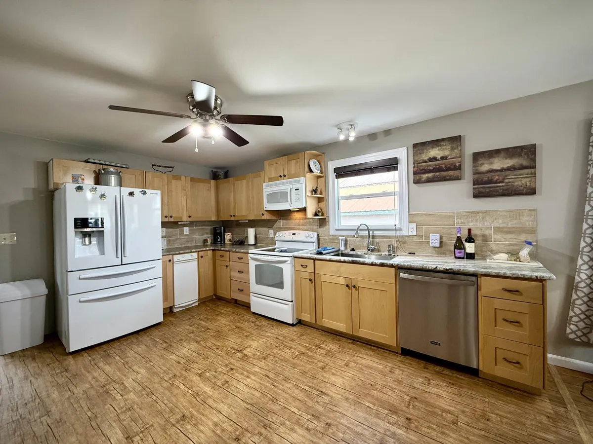 A stylish kitchen fitted with stainless steel appliances, wood cabinets, a kitchen island, and a window letting in natural light. The arrangement is practical and visually appealing, emphasizing generous counter space and a welcoming environment for cooking and food preparation.